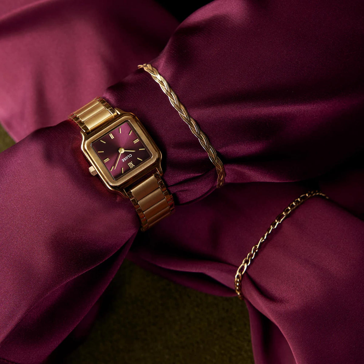 Gold-tone square watch with purple-red dial on satin fabric, metal link bracelet