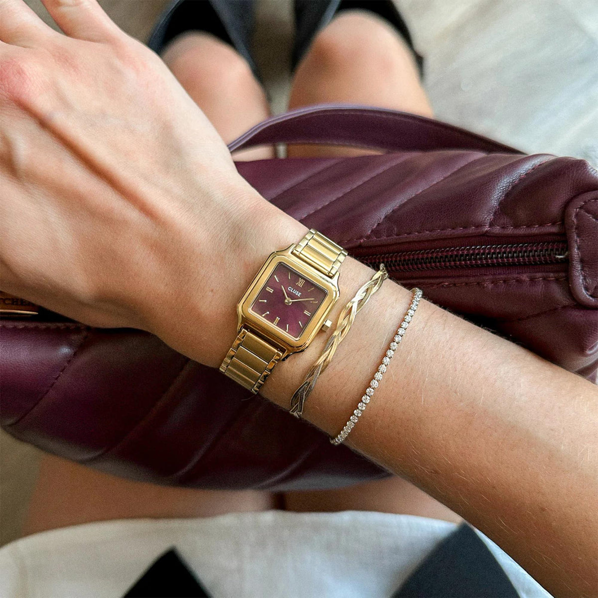 Gold-tone steel strap quartz watch with purple-red dial on wrist