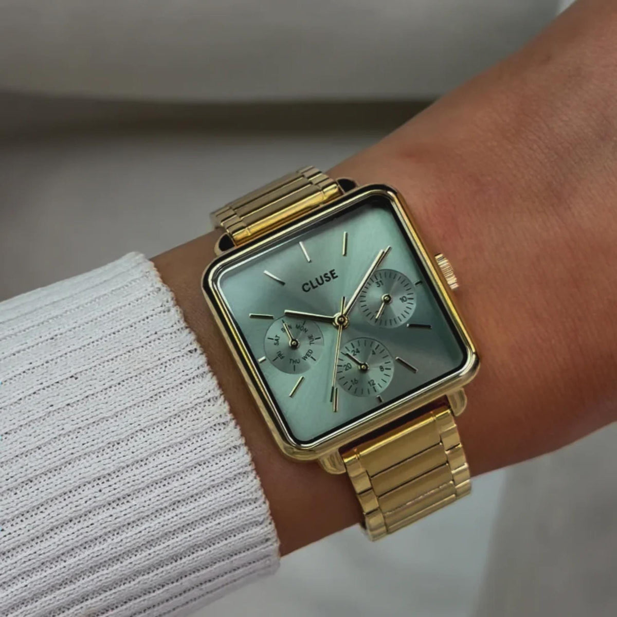 Gold-tone square chronograph watch on wrist, light green dial with three subdials