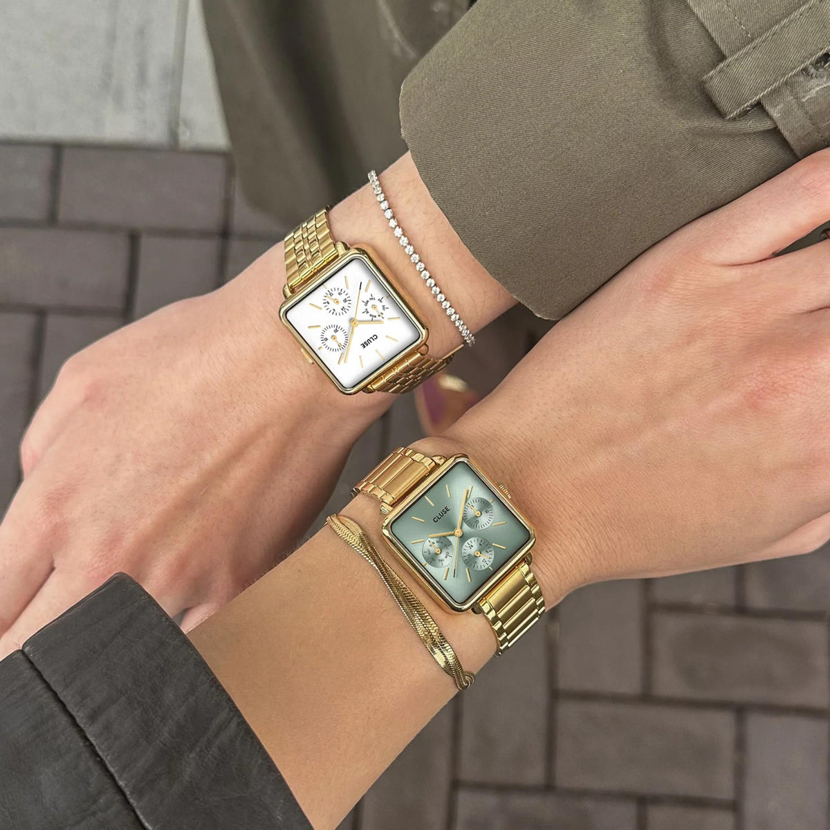 Two square gold-tone watches on wrists with bracelet straps, one pale dial and one blue dial