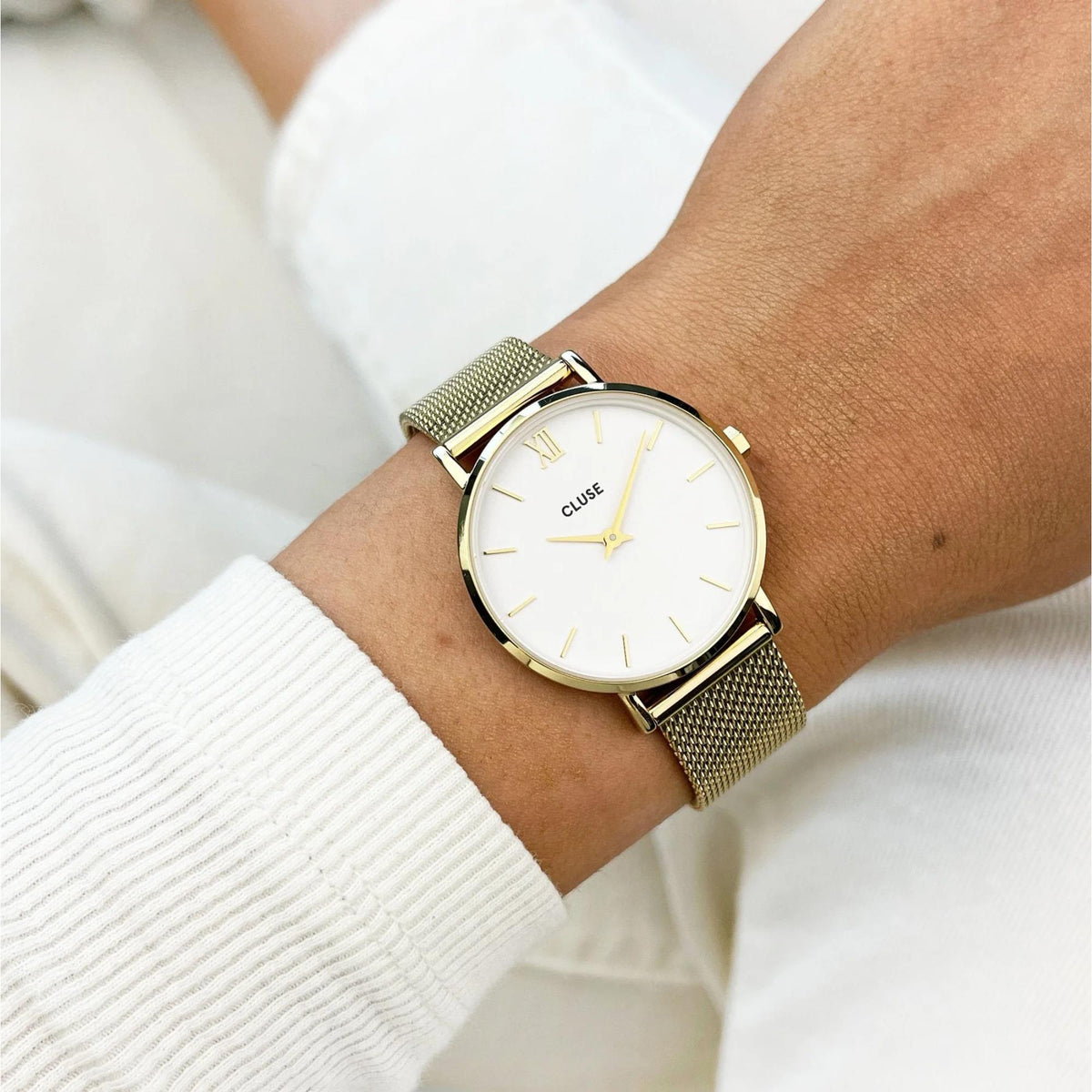 Gold-tone women’s quartz watch on wrist with white dial and mesh bracelet, gold hour markers