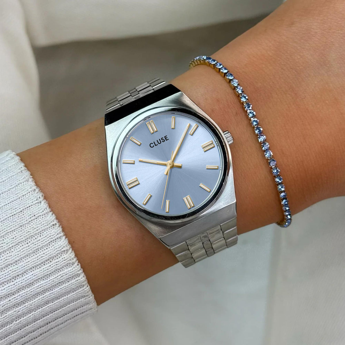 Women's steel watch with light blue dial, gold markers and hands, on wrist