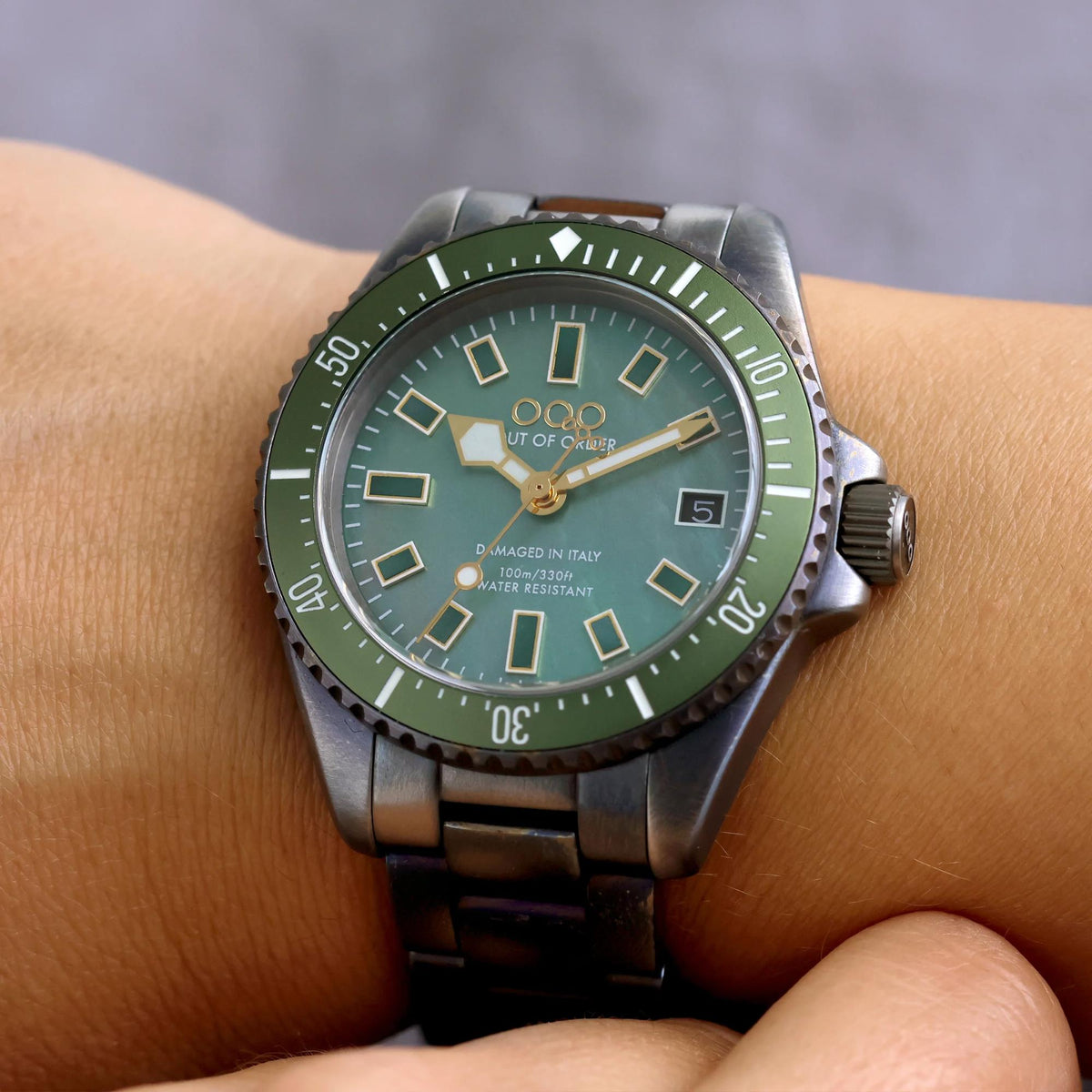 Green dial steel strap watch with gold markers, three-hand analog display, round case