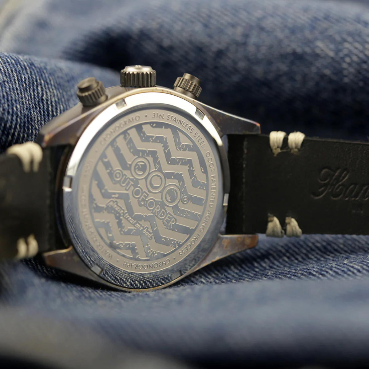 Stainless steel watch case back with engraved markings and black leather strap