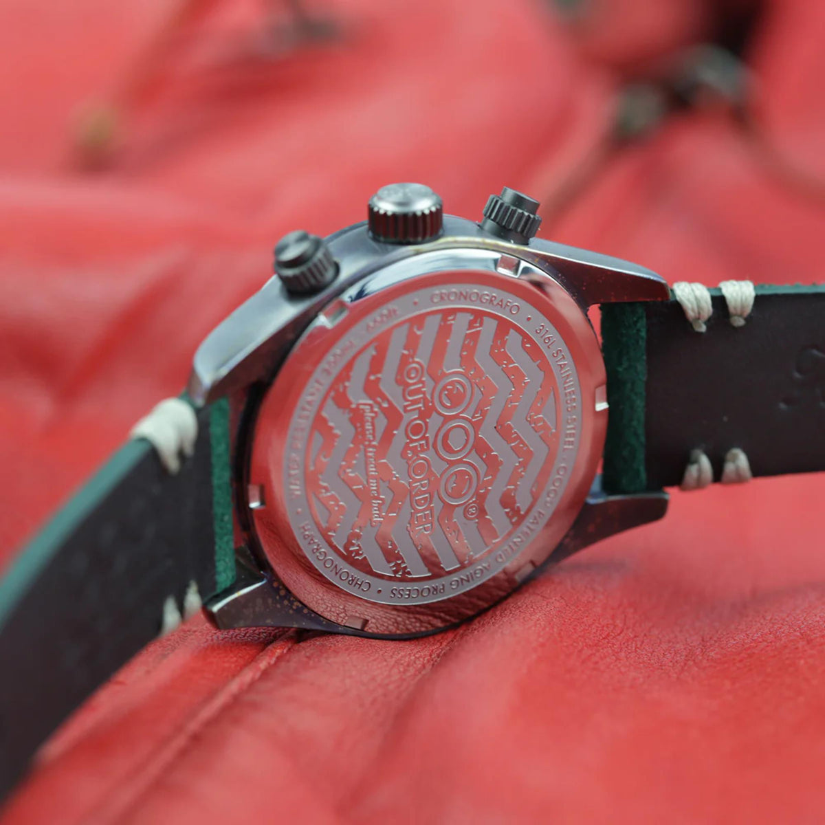 Men's sporty watch caseback with engraved pattern and side crowns, green leather strap.