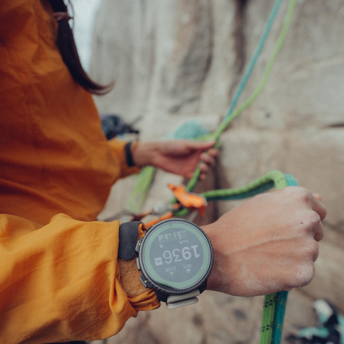 Climber wearing the Suunto Vertical Titanium Solar Sand watch while handling climbing ropes against a rock wall background