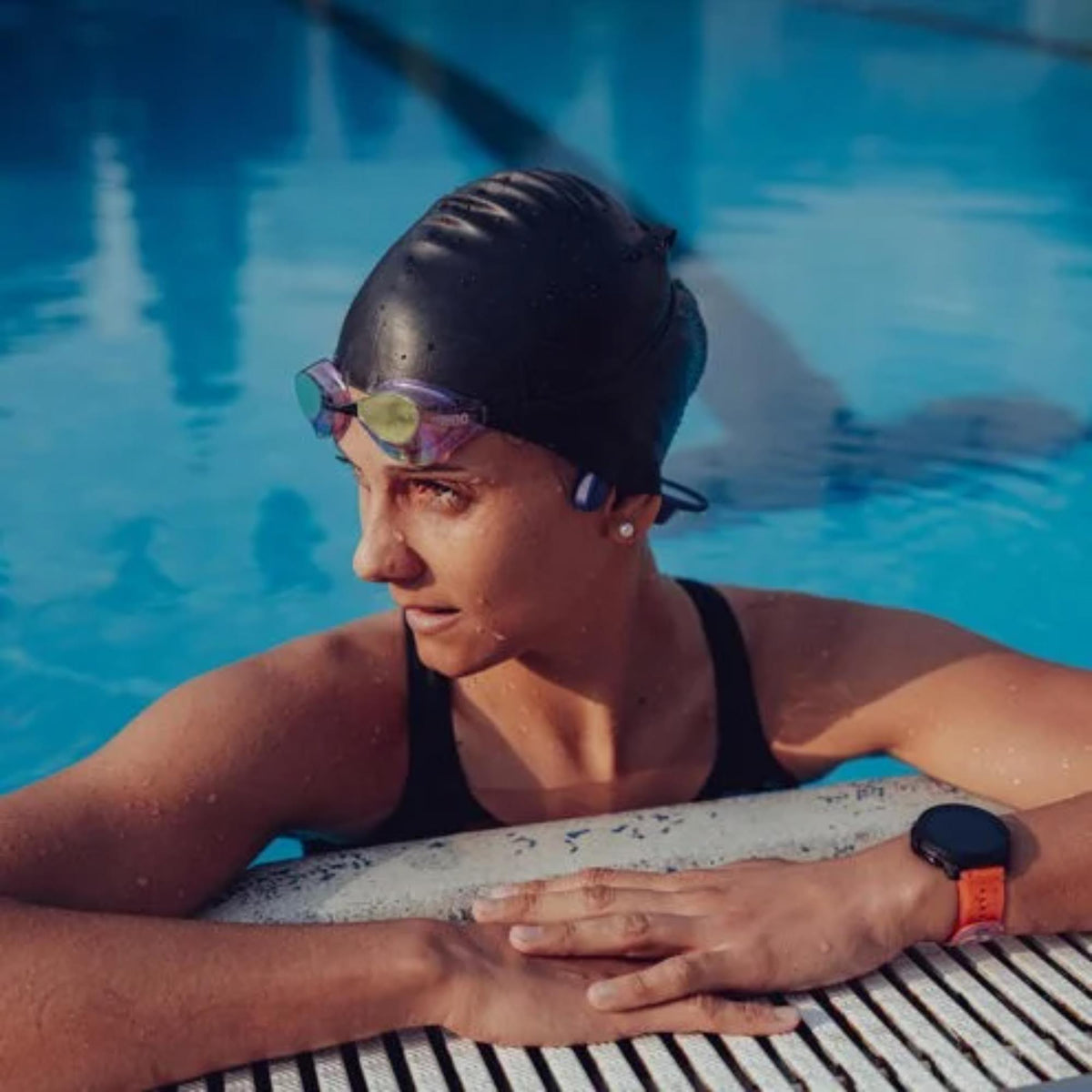 Suunto Aqua SS051124000 light tidal black sports open-ear wireless headphones lifestyle image of swimmer at pool edge wearing sports watch with orange strap