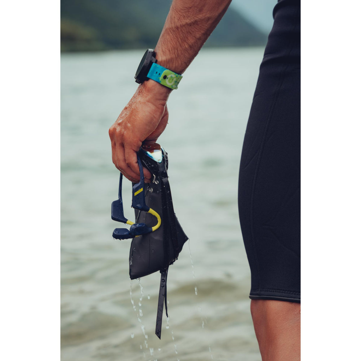 Suunto Aqua SS051108000 lime blue sports open-ear wireless headphones held alongside swim cap water sports equipment