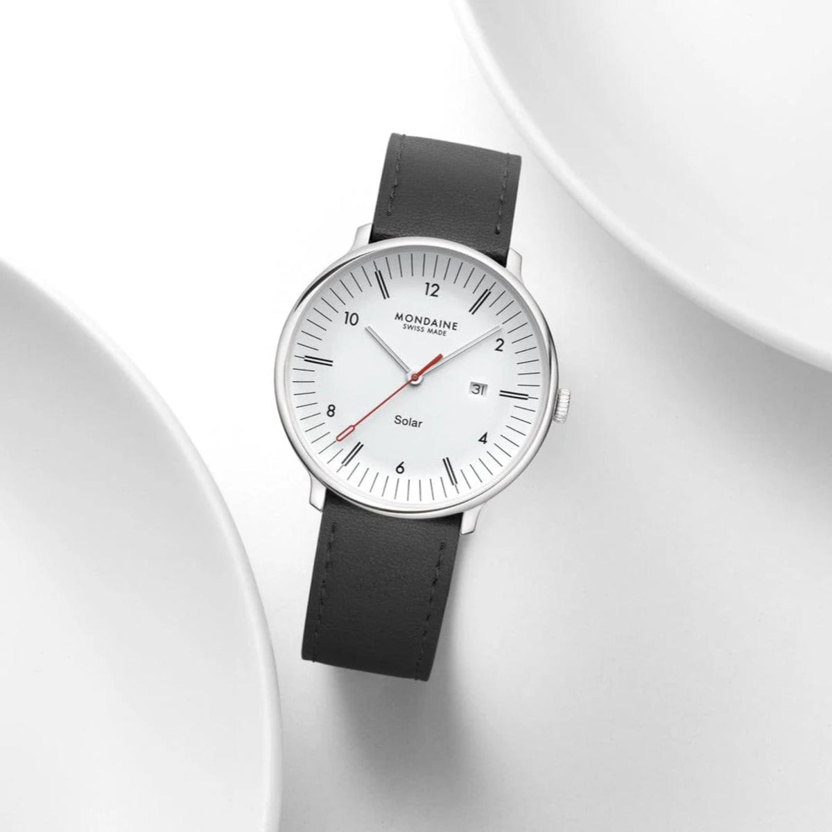 The Mondaine Doppio solar mens watch displayed elegantly from a top-down angle between two clean white ceramic plates