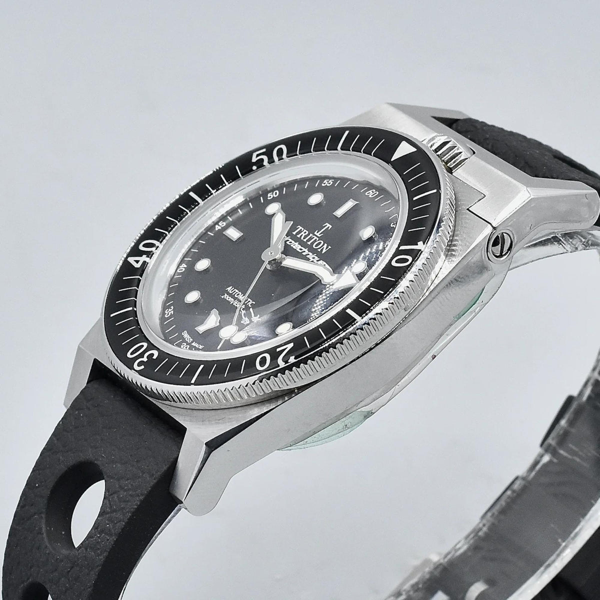 Men's dive watch angled view, black dial, steel case with textured bezel, black rubber strap.