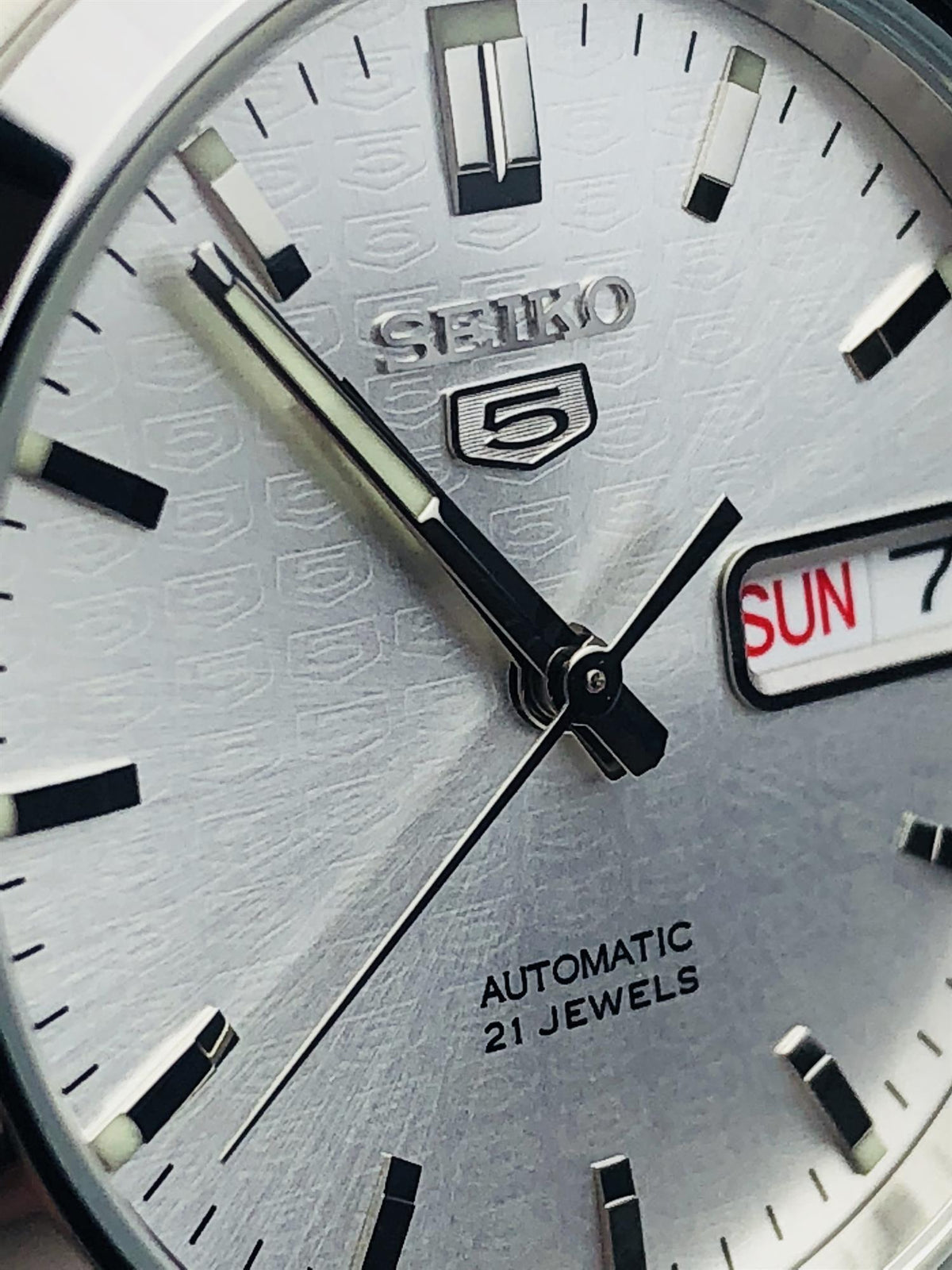 Close-up view of the Seiko 5 SNK355K1 watch dial highlighting the repeating embossed shield pattern and day-date window