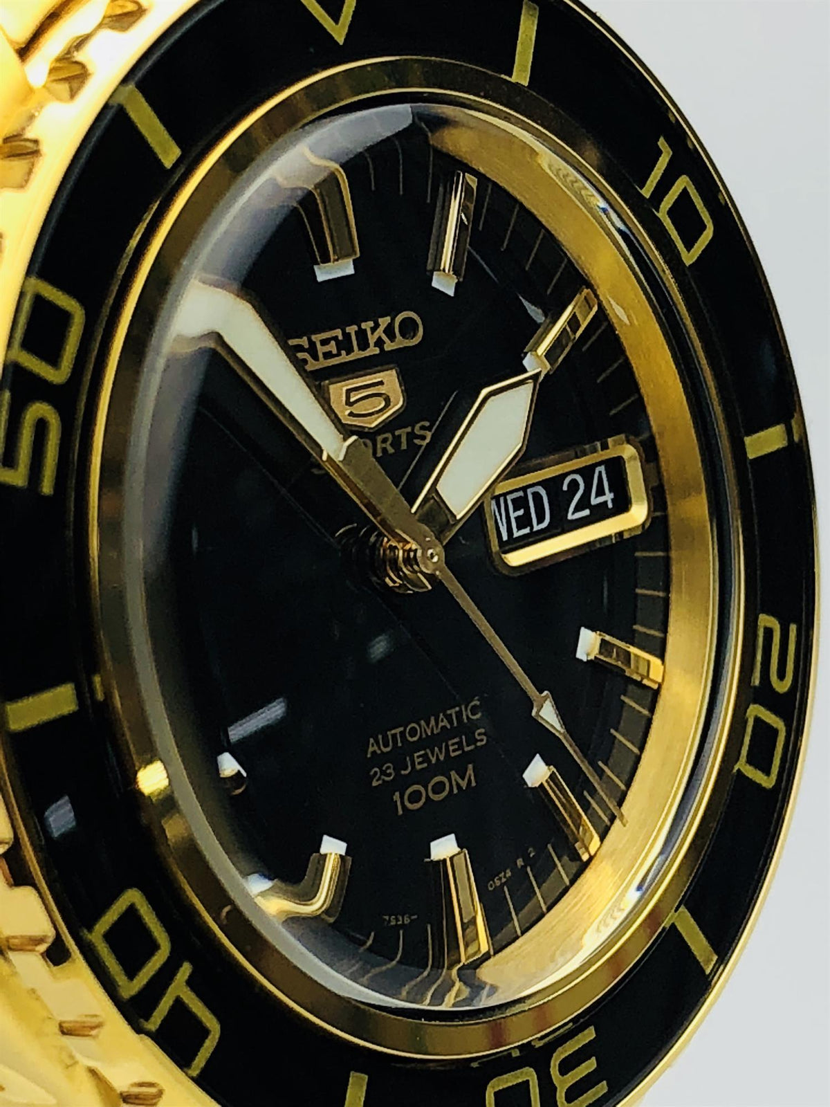 Close-up of gold-accent black dial with hands and date window reading WED 24