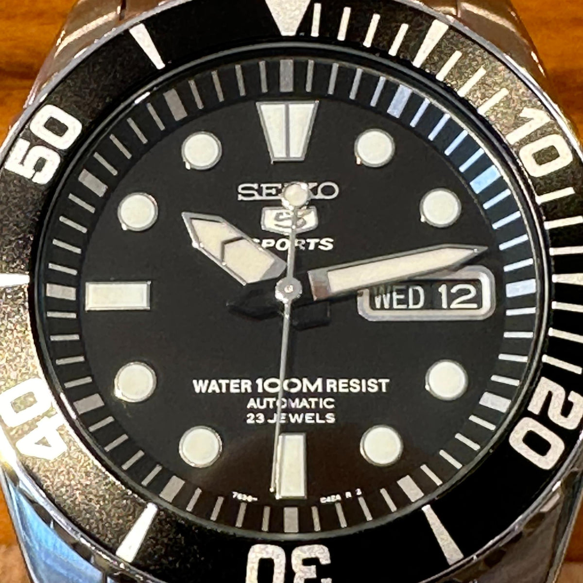 Seiko Sports black dial watch close-up with WED 12 date window and silver dive-style bezel