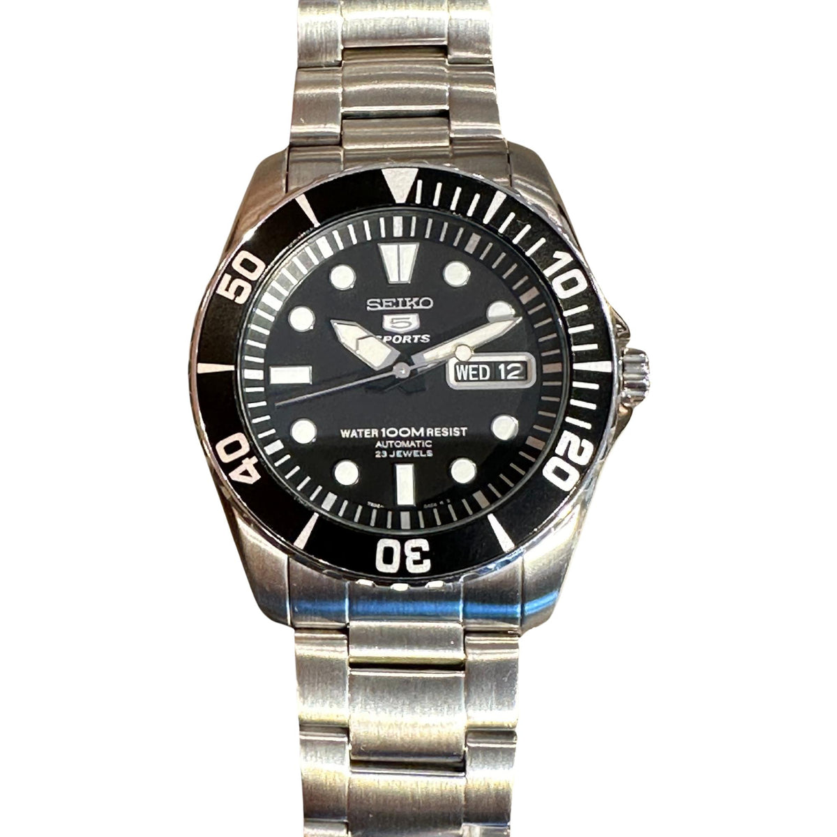 Men's black-dial Seiko Sports automatic watch on stainless steel bracelet, showing WED 12