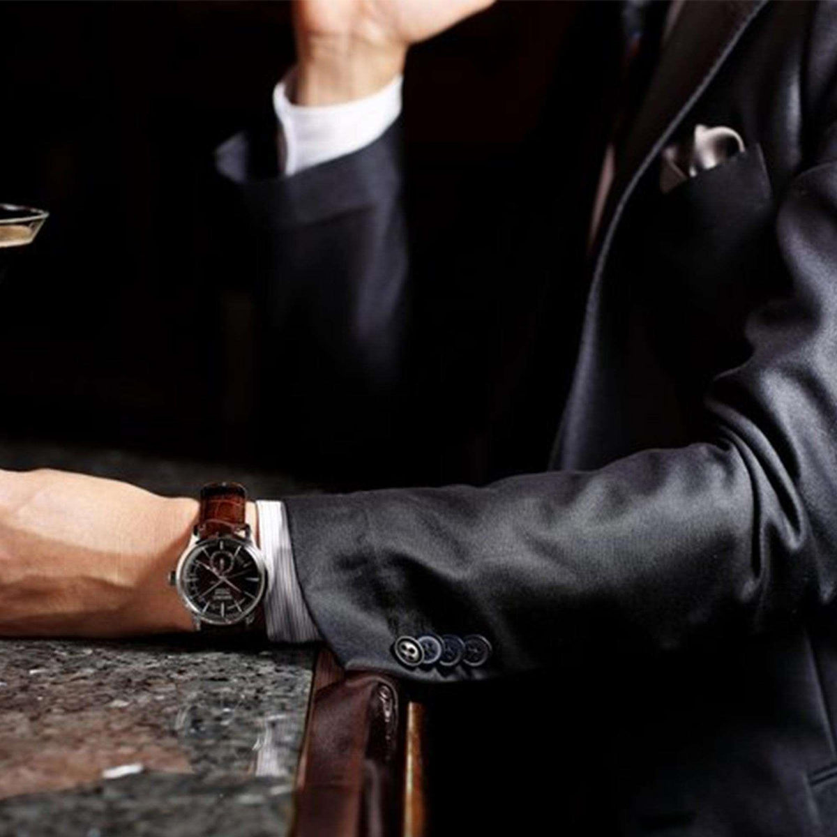 Men's auto watch on wrist, brown leather strap, dark dial, at shirt cuff