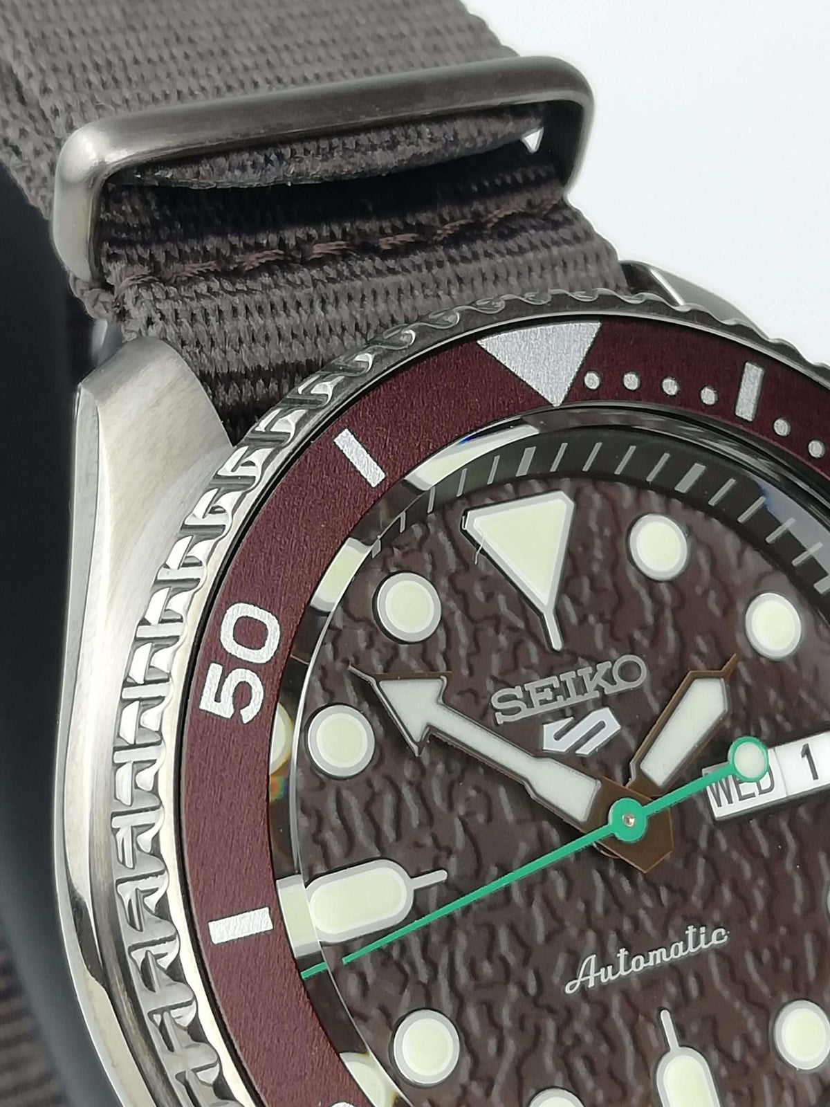 Seiko 5 Sports close-up of dial and bezel: brown dial, green-accent hands, date display