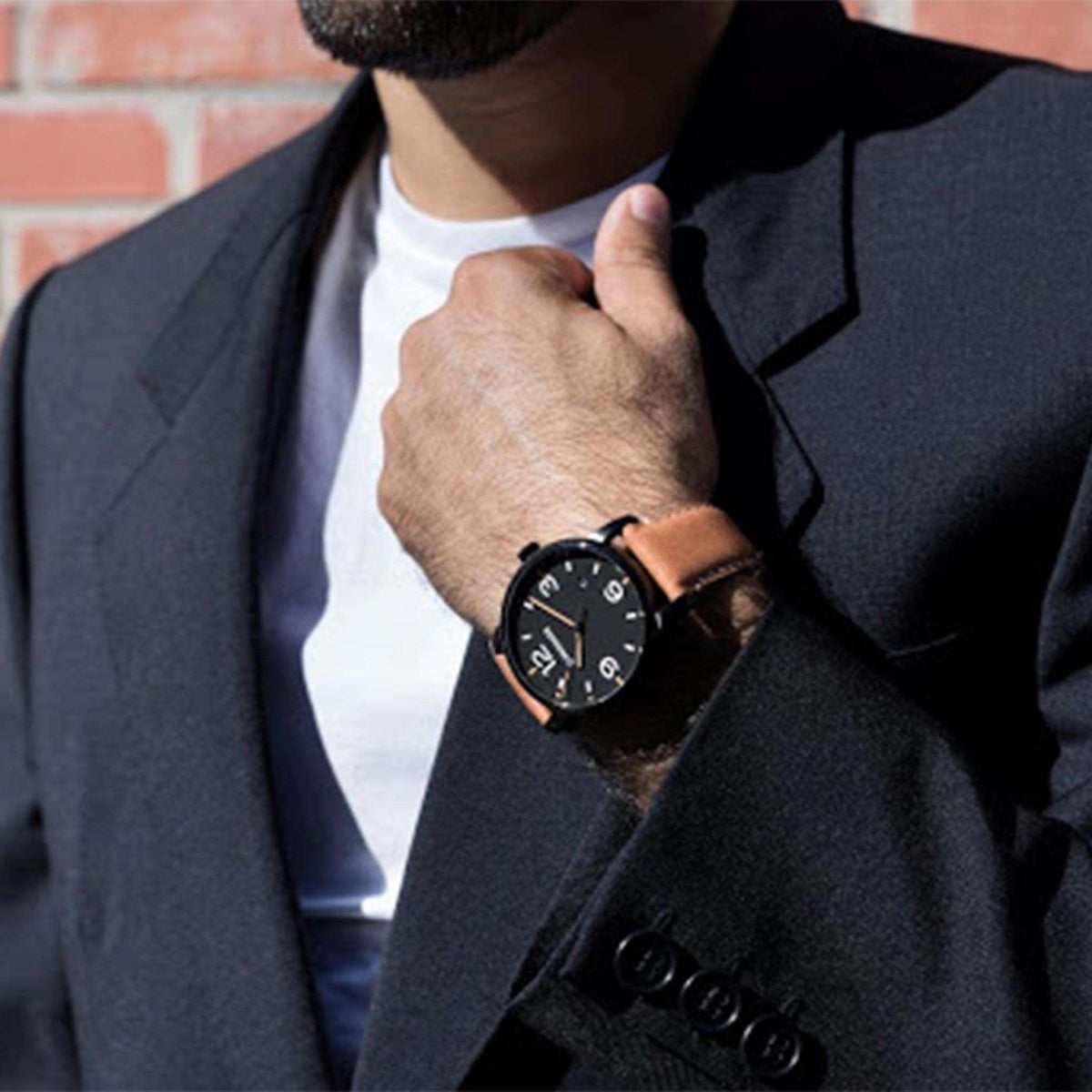 Men's wrist watch under jacket sleeve, black dial with orange markers, brown leather strap.