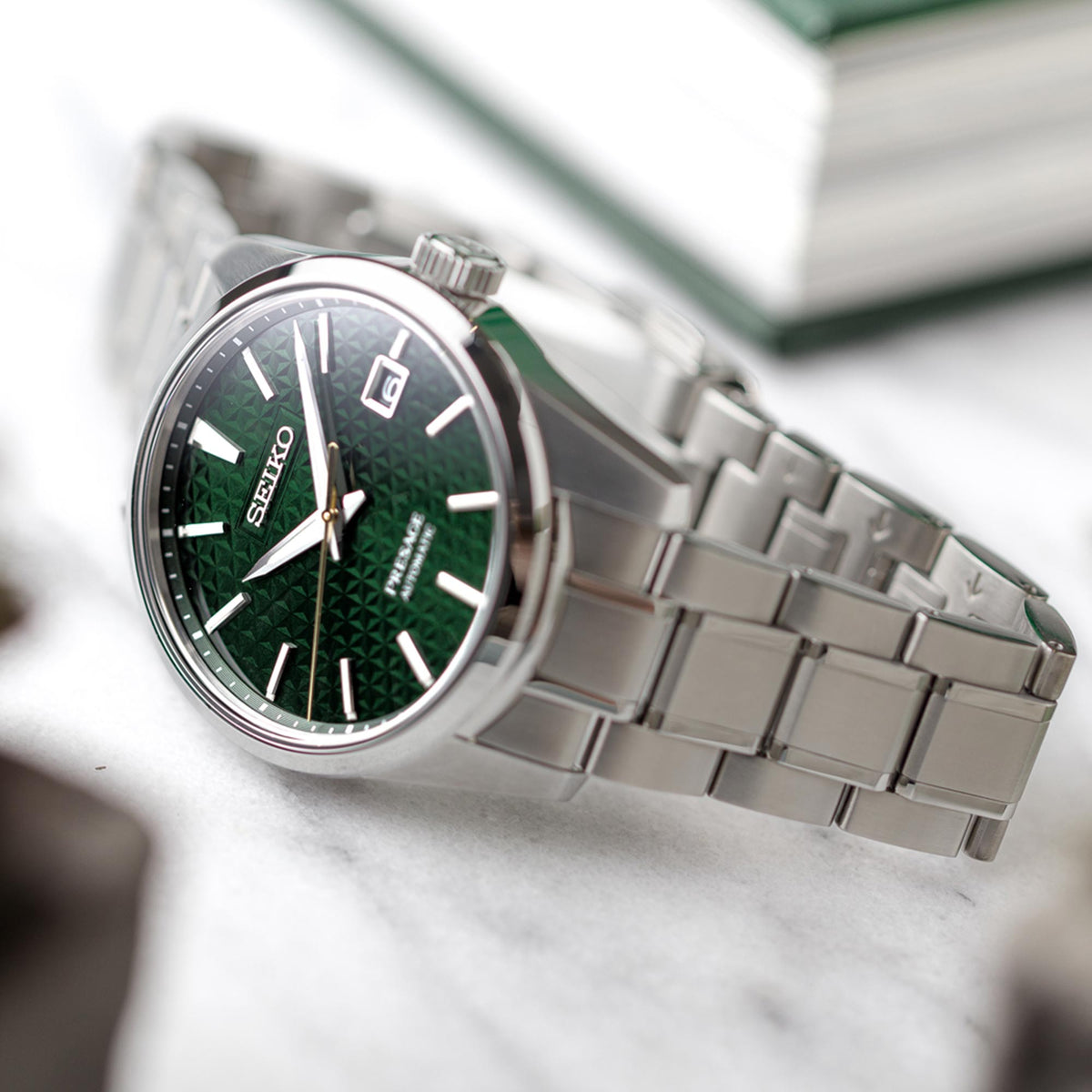 Men's automatic wrist watch with green dial and silver stainless bracelet, angled close-up