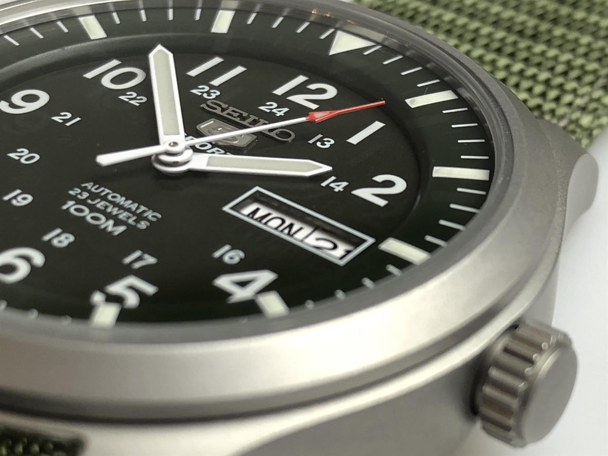 Men's green dial watch close-up showing hour marks and MON date window