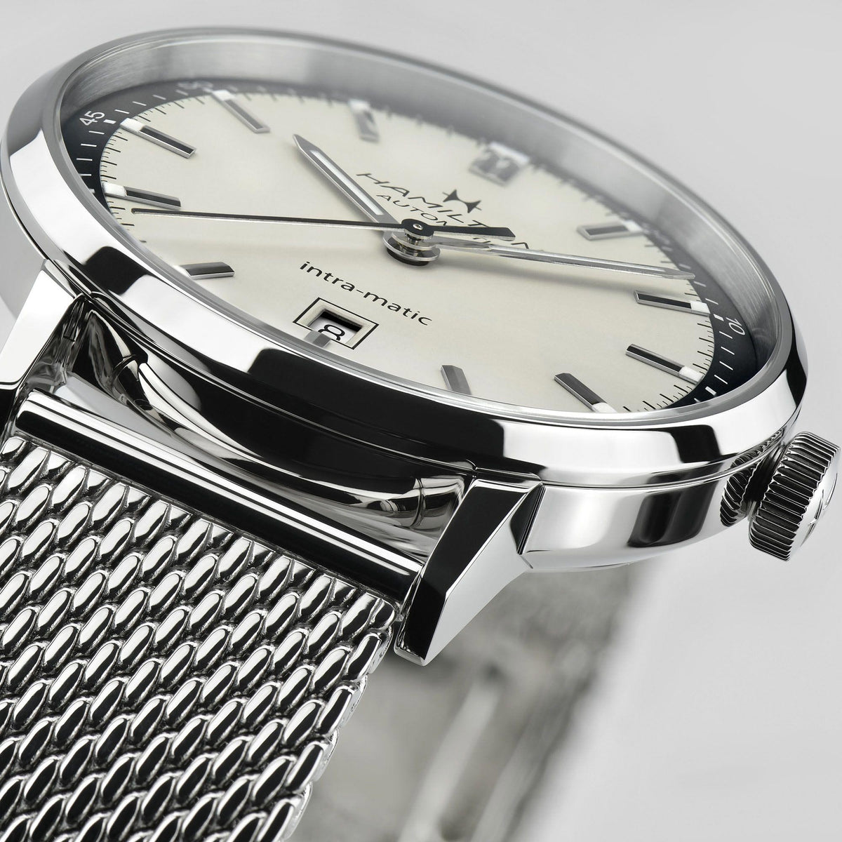 Close-up view of men's automatic watch, reflective steel case, white dial with hands and markers