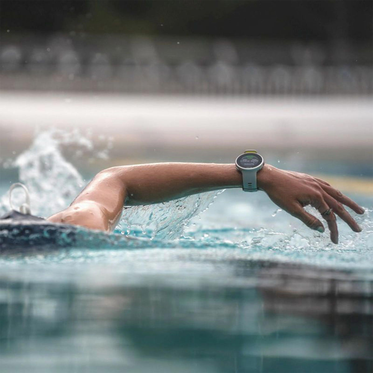Grey rubber-strap smartwatch on wrist in pool water with display visible