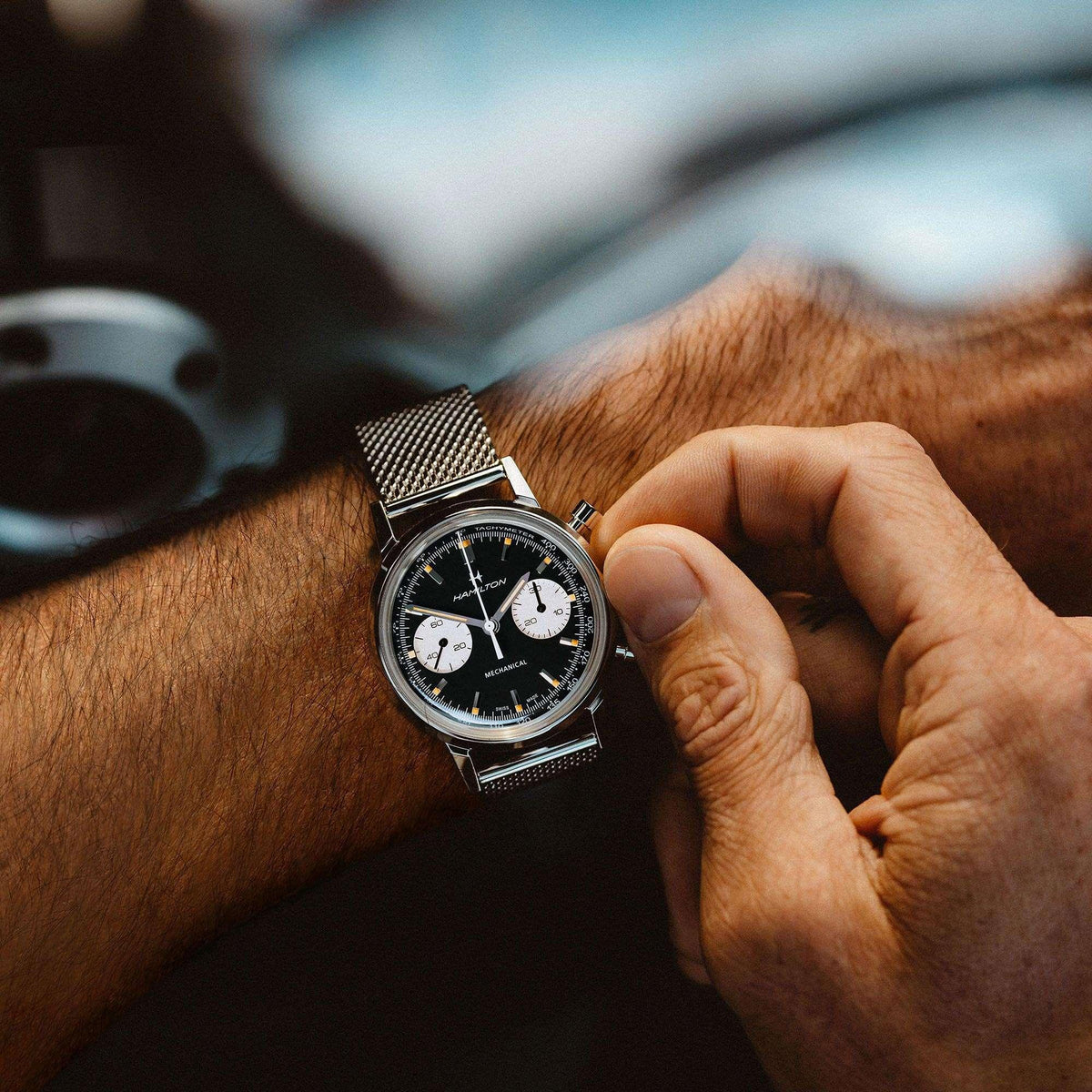 Men's steel mesh chronograph watch on wrist with black dial and white subdials