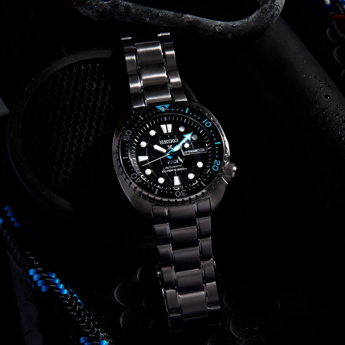 Dive watch on stainless steel bracelet with black dial, blue hands, and date window