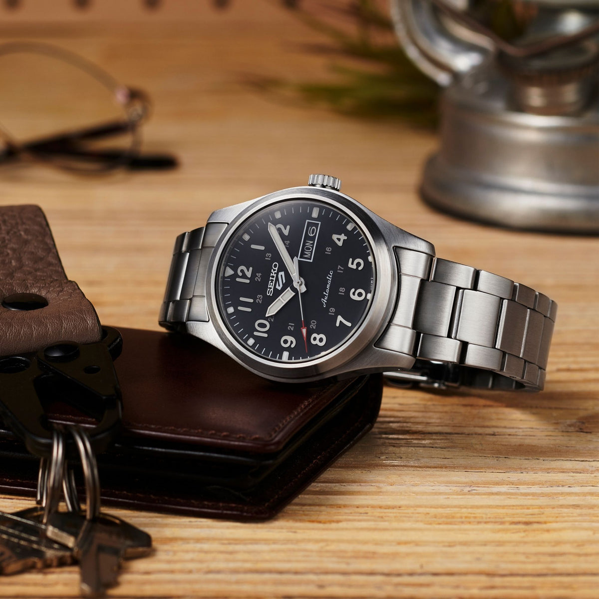 Seiko men’s watch on leather surface with black dial and stainless bracelet, side angle