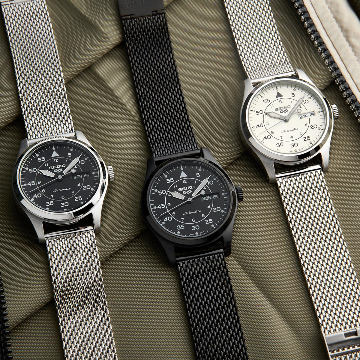 Three Seiko watches with mesh straps on a textured surface