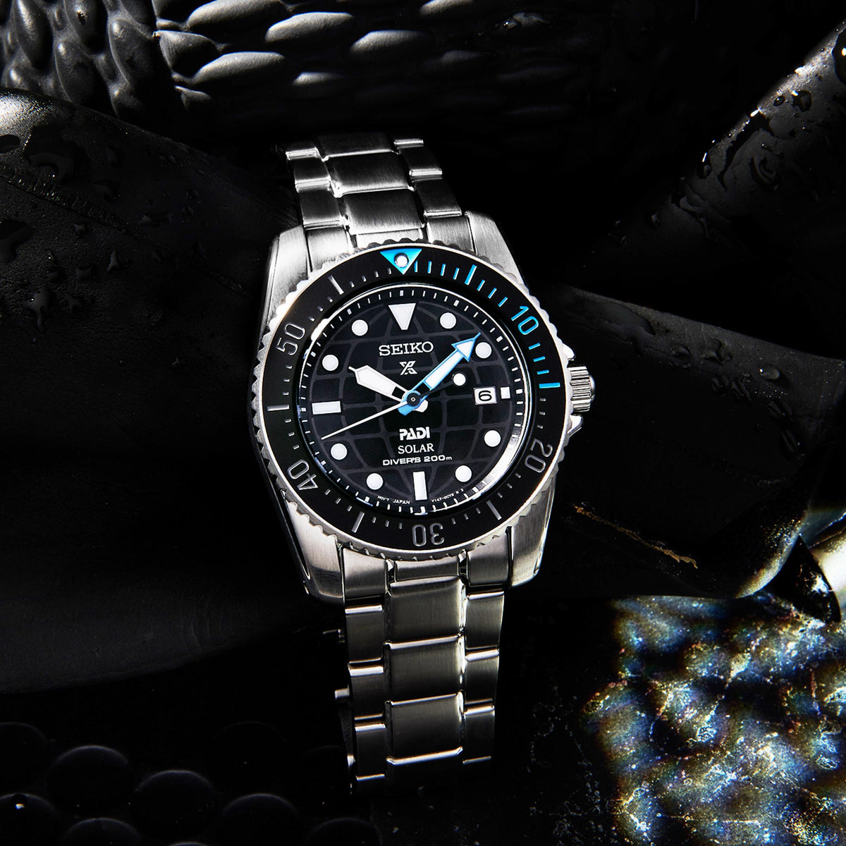 Stainless steel dive watch with black dial and blue bezel stripe, solar text, bracelet.