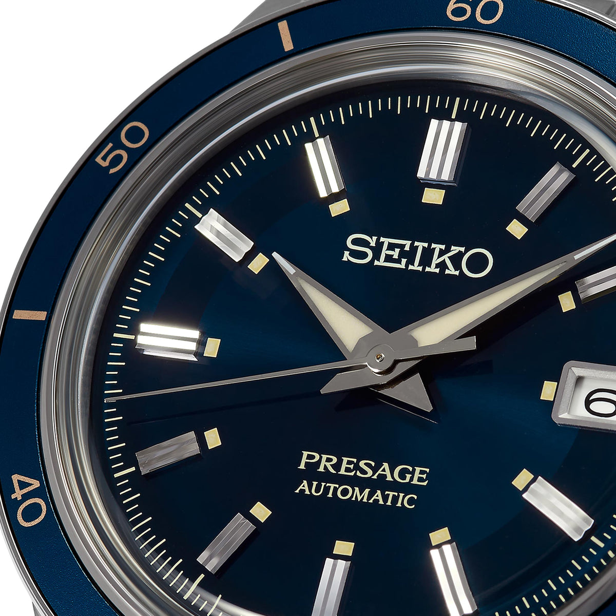 Close-up of blue watch dial with bold hour markers, gold-tone hands, and date window