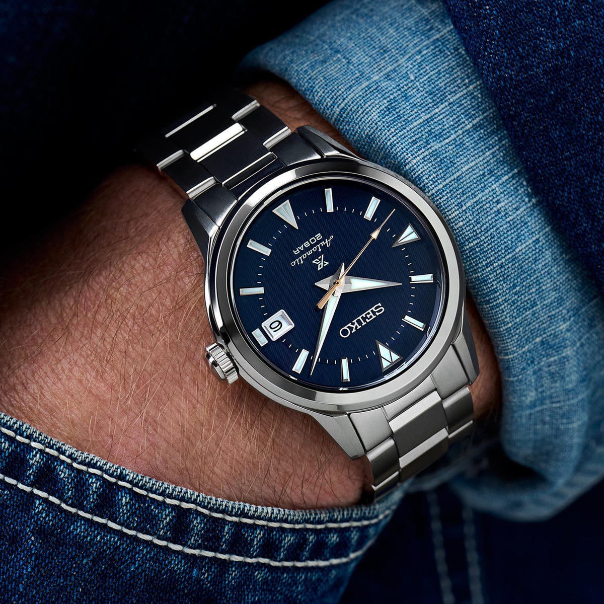 Men's stainless steel automatic watch on wrist with blue dial, metal bracelet, date window
