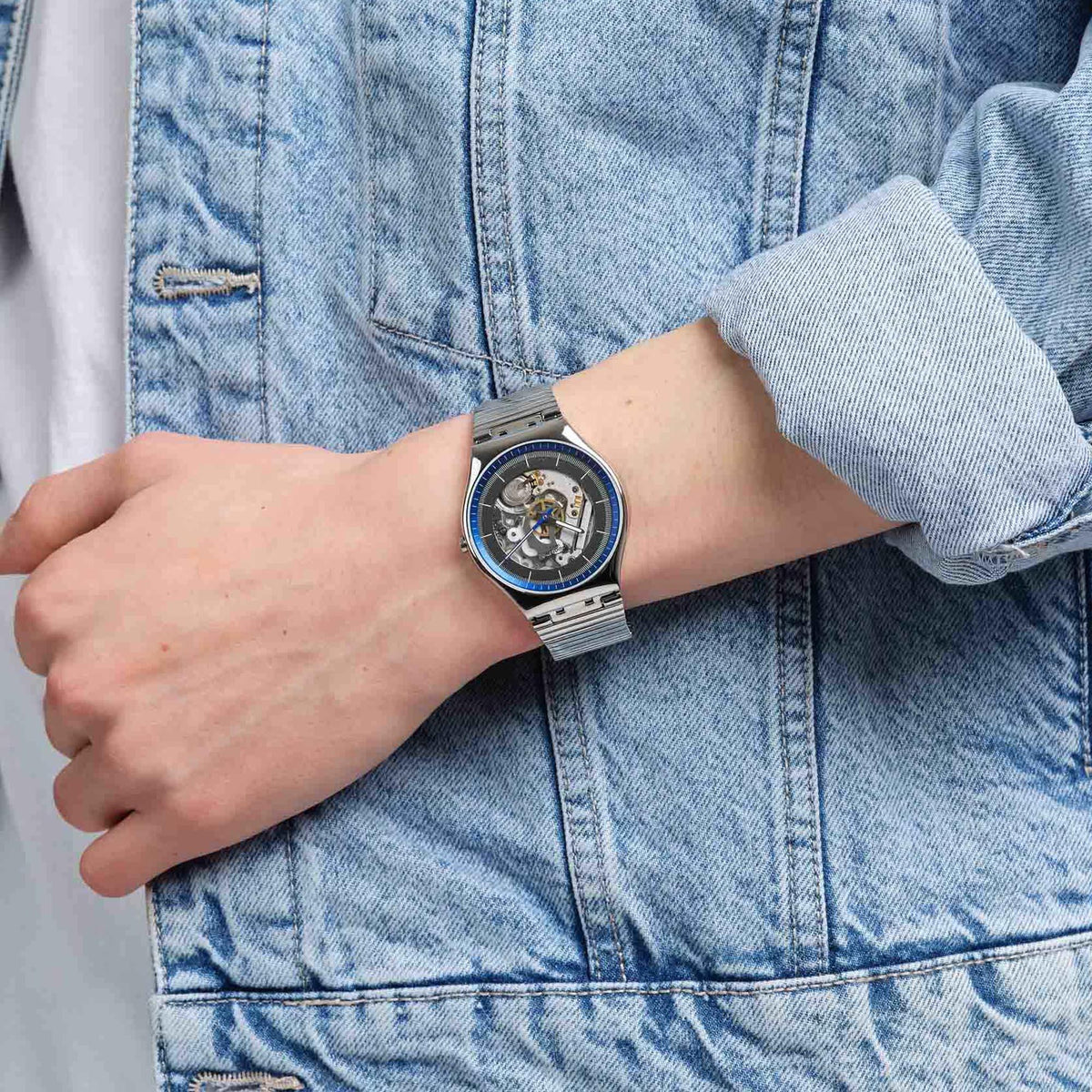 Swatch stainless steel watch on wrist with blue bezel and exposed skeleton dial