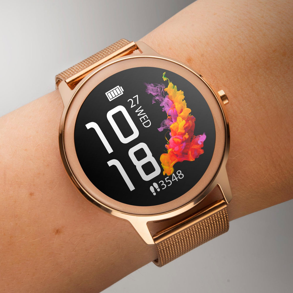 Rose gold smartwatch on wrist with mesh band and round black face showing 10 and 18