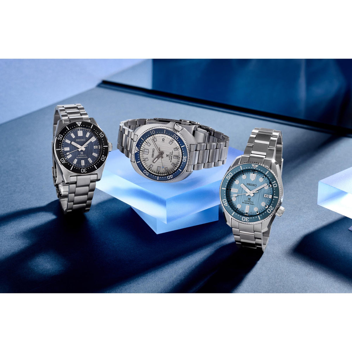 Three stainless steel diver watches with black, blue, and silver-white dials