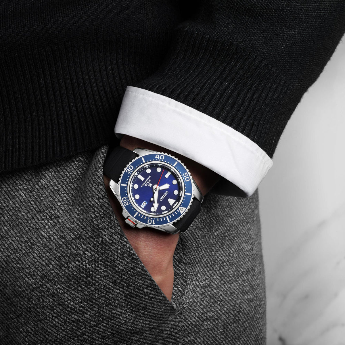 Men's solar diver watch on wrist with blue dial, black rubber strap, white shirt cuff