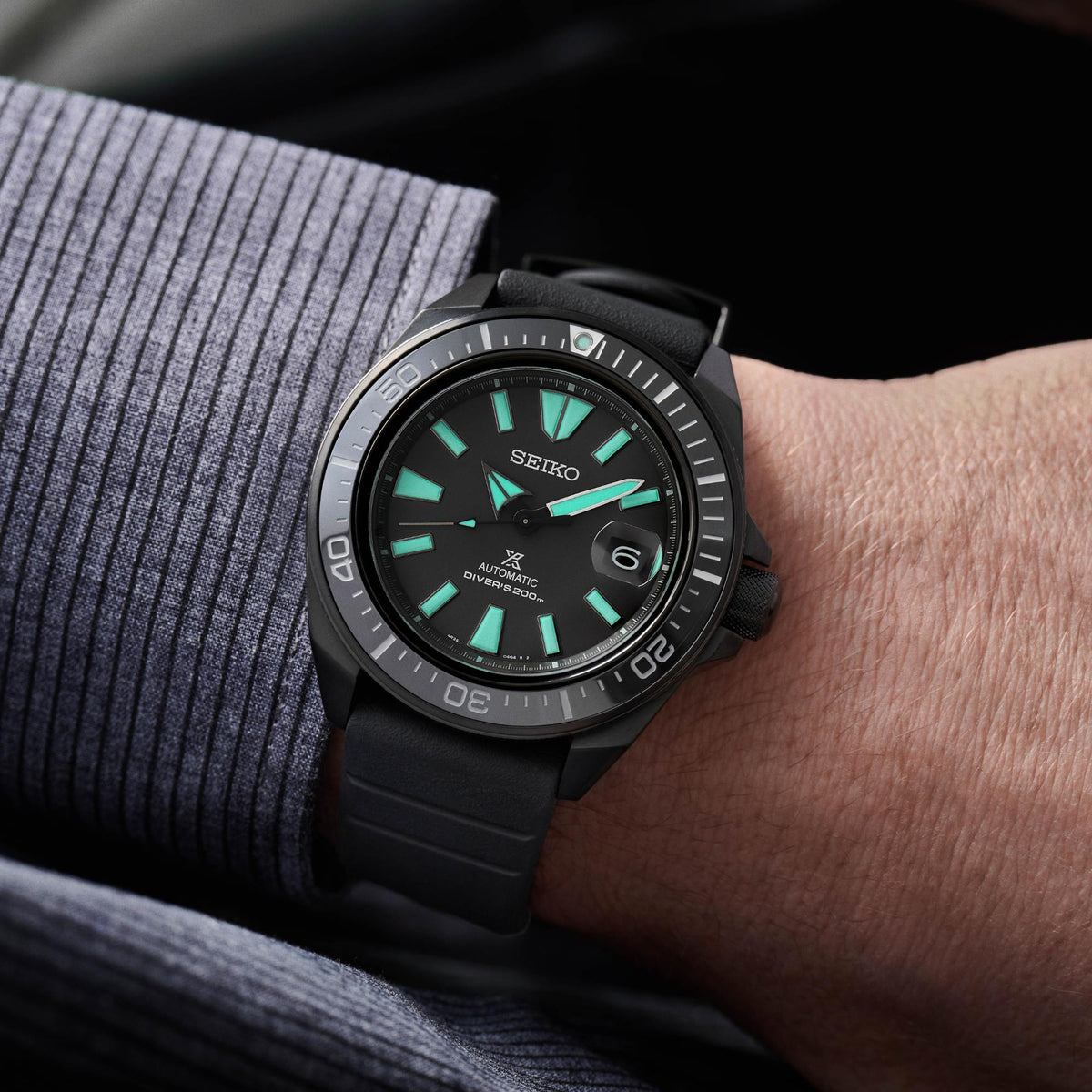 Seiko diver watch worn on forearm, black strap with green hour markers