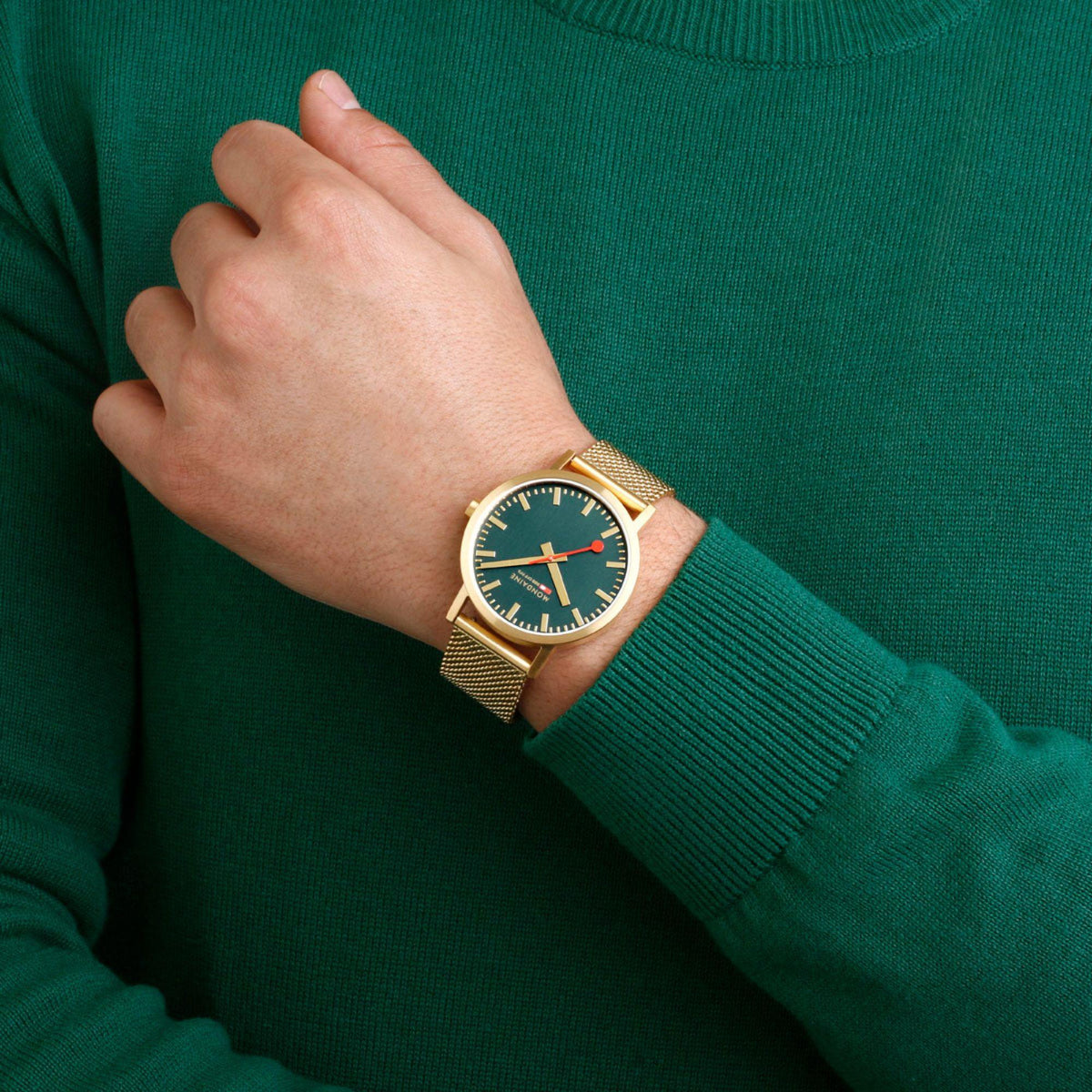 Gold-tone mesh bracelet watch on wrist with green dial and red seconds hand