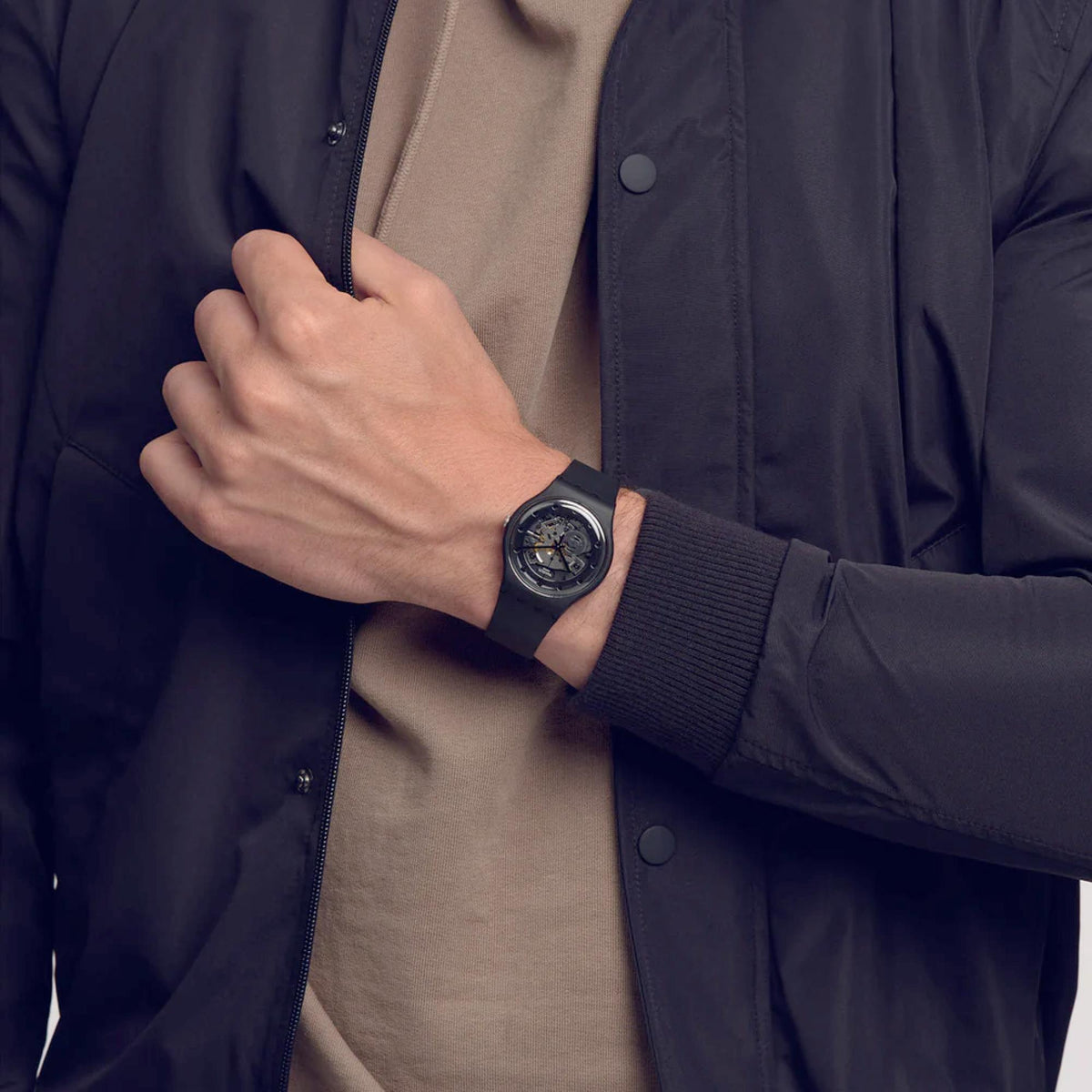 Quartz watch on wrist with dark rubber strap and skeleton dial, worn with blue jacket sleeve