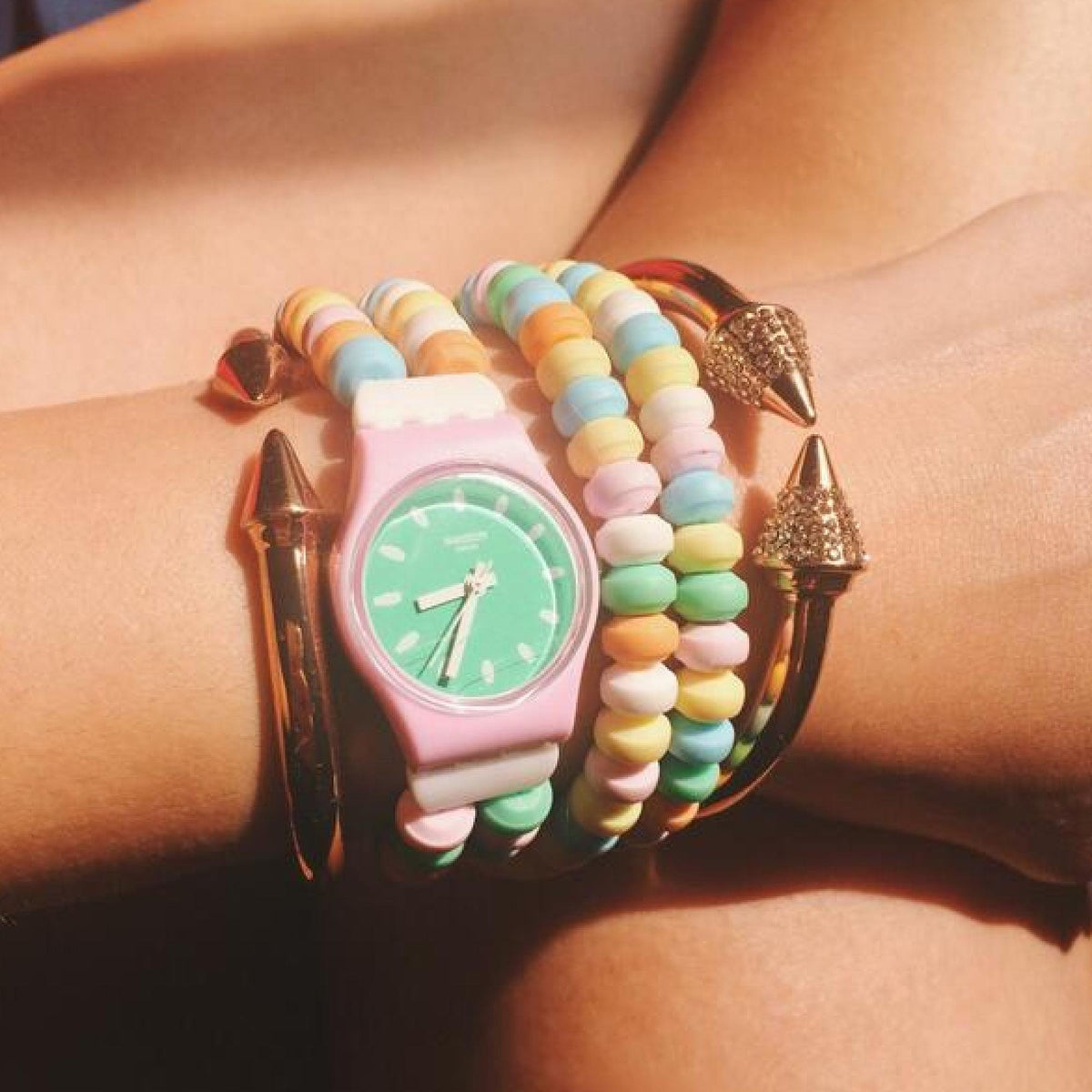 Green-dial ladies watch on wrist, pink strap with pastel beaded bangles and gold bracelets