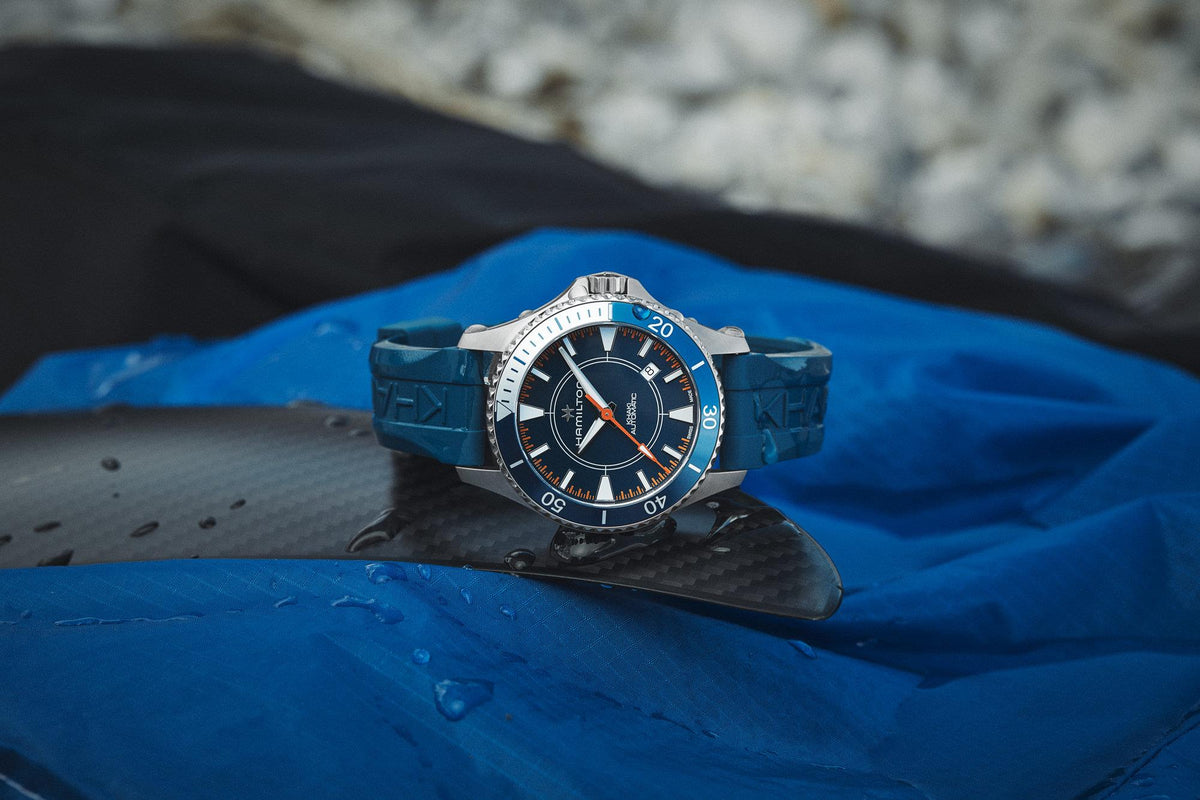 Men's automatic watch with blue dial, orange-accent bezel, and blue rubber strap.