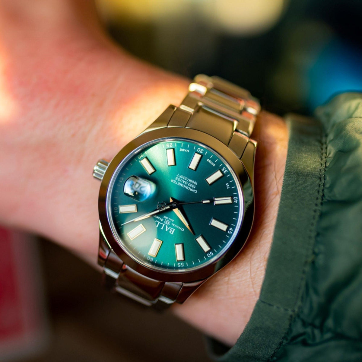 Men's wrist watch close-up on wrist, dark green dial with luminous markers and crown detail.