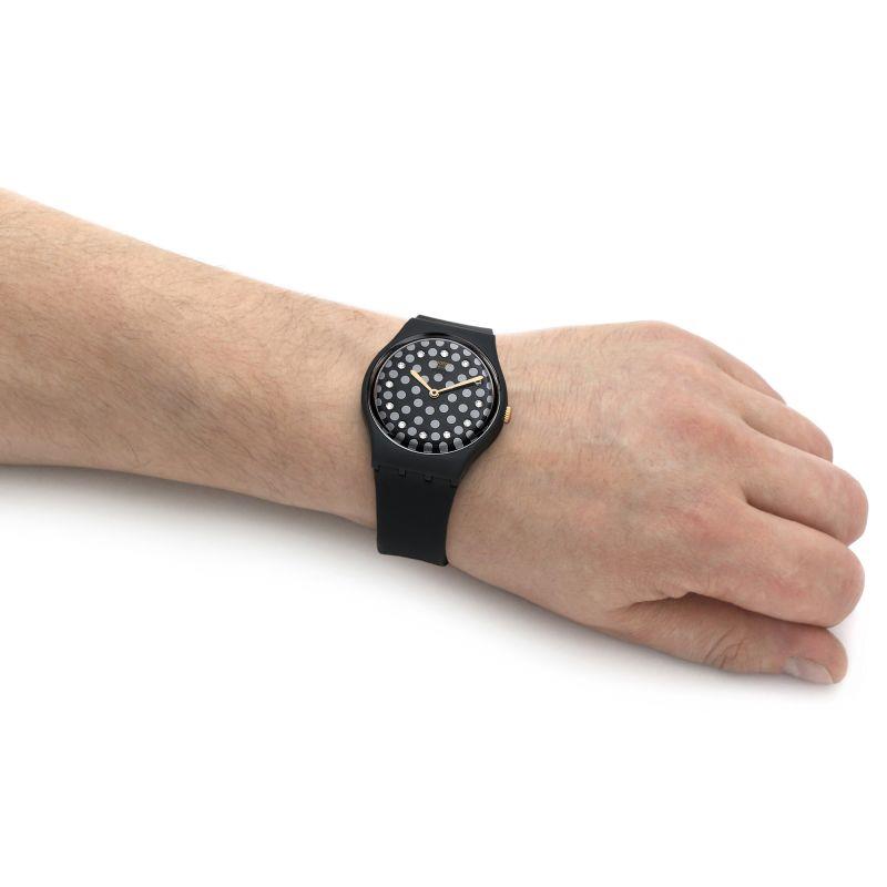 Swatch black rubber watch on wrist, round speckled dial with gold-toned hands.