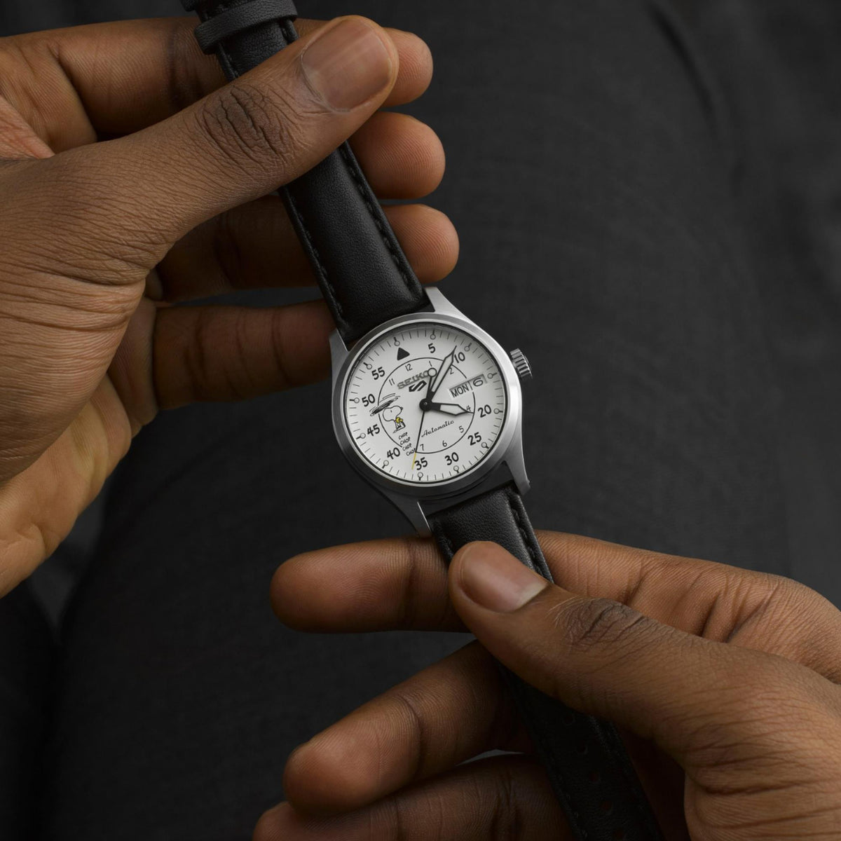 Automatic white dial wristwatch with black leather strap held in hands, round steel case