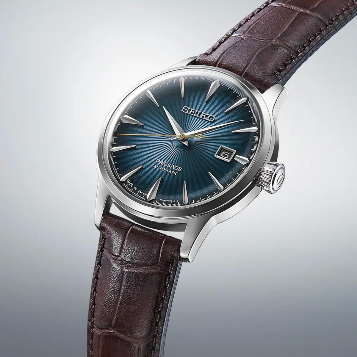 Men's automatic watch with dark blue sunburst dial and brown leather strap, angled view.
