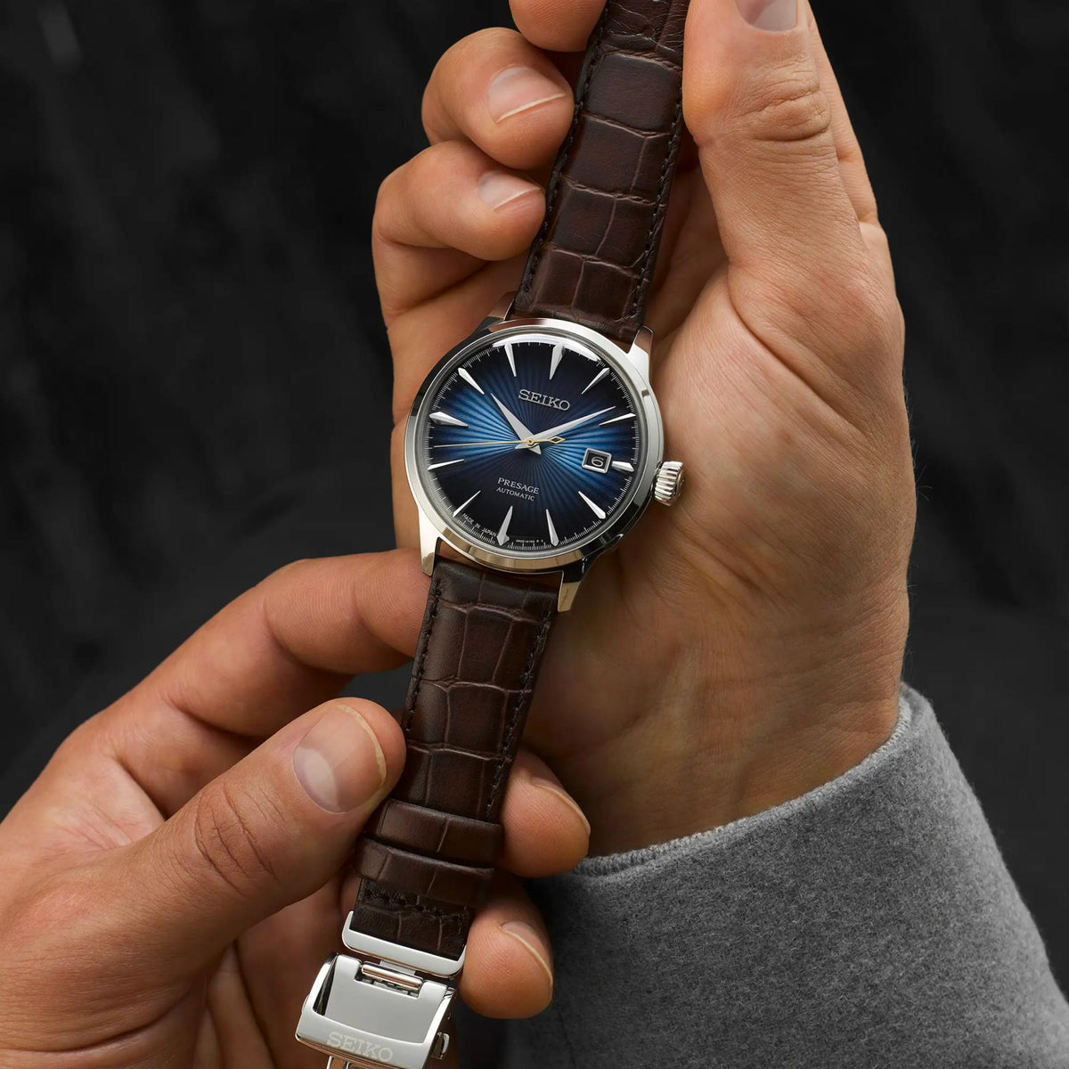 Men's automatic watch on wrist with brown leather strap and dark blue dial.