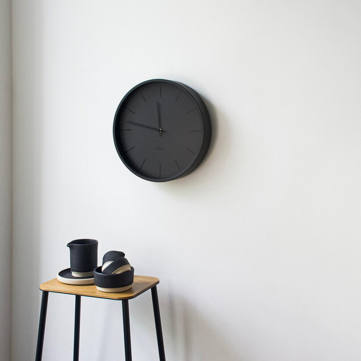 Black round wall clock with slim markers and three hands, mounted on a wall