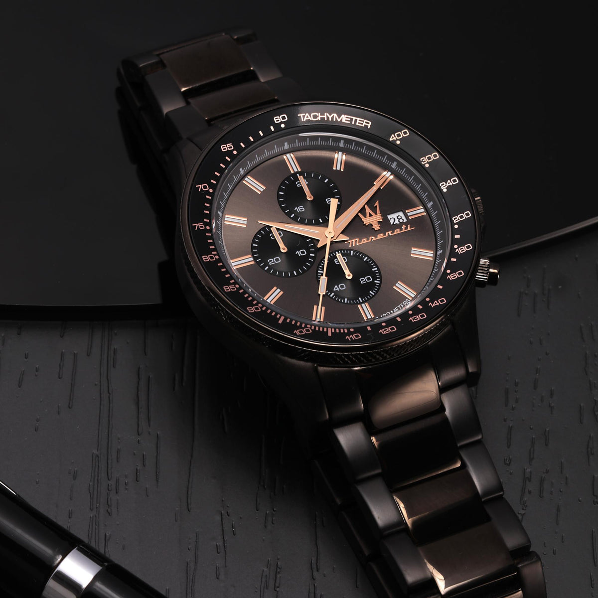 Black chronograph watch with tachymeter markings, rose-gold hands, and pushers