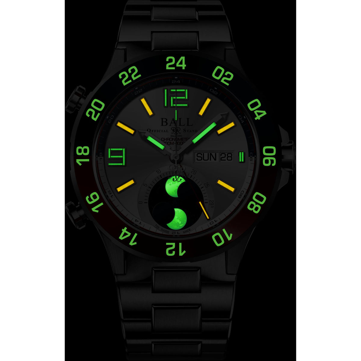 Black watch with green glowing hands and hour markers, moon-phase subdial, metal bracelet.