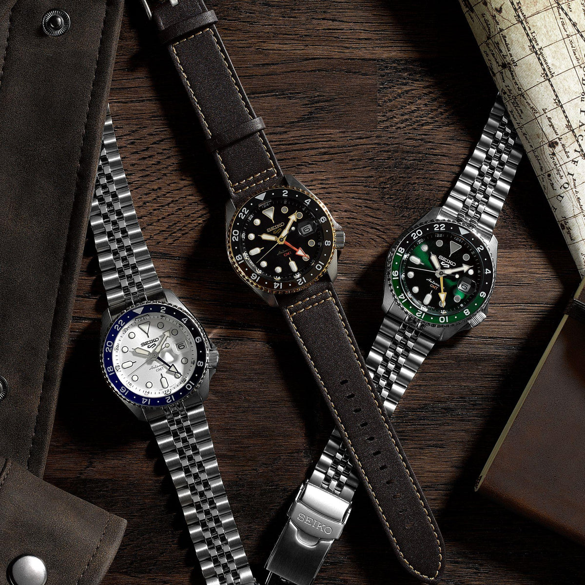 Set of men’s watches on wood; brown-leather black-dial GMT watch visible.